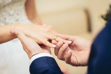 Eine Person im Anzug schiebt einer anderen Person im Hochzeitskleid einen Ring auf den Finger
