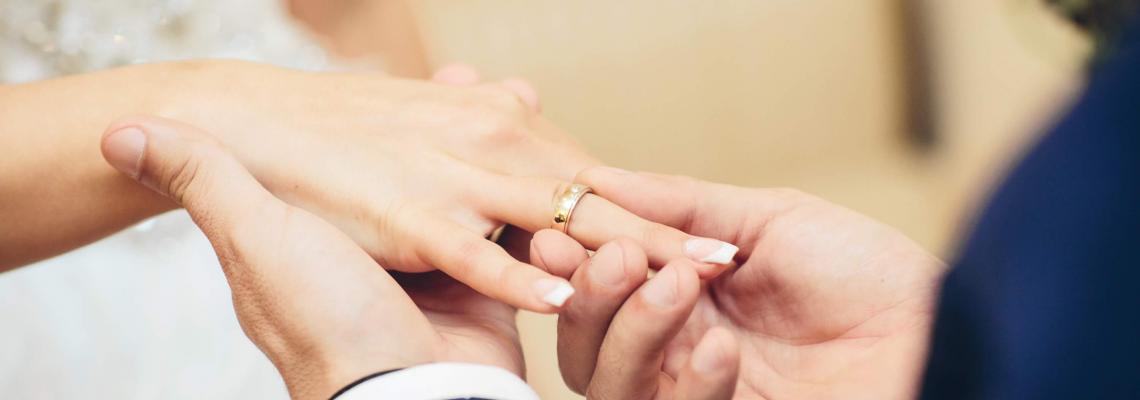 Eine Person im Anzug schiebt einer anderen Person im Hochzeitskleid einen Ring auf den Finger